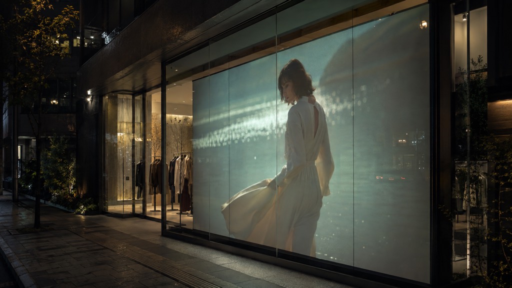 夜のアパレル店舗。ガラス窓にブランドムービーが投影され、店内の商品が透けて見えるコンセプト画像