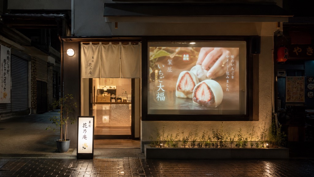 夜の小さな和菓子店。一枚の窓にいちご大福のPR映像が投影されているコンセプト画像